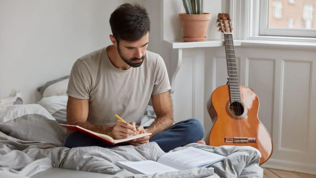 Man sitting on bed writing in a journal