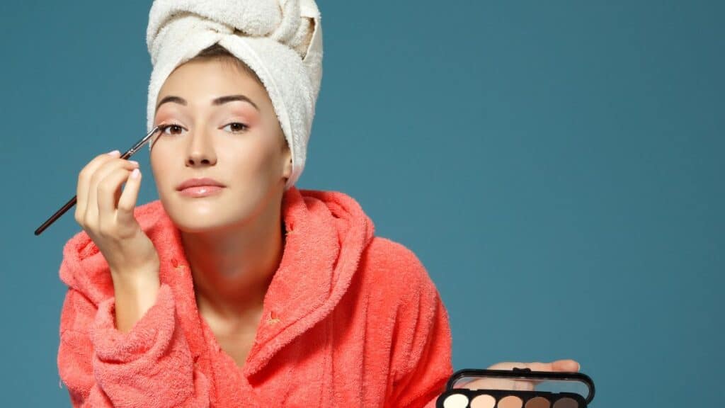 Woman in a robe and towel on her head putting makeup on