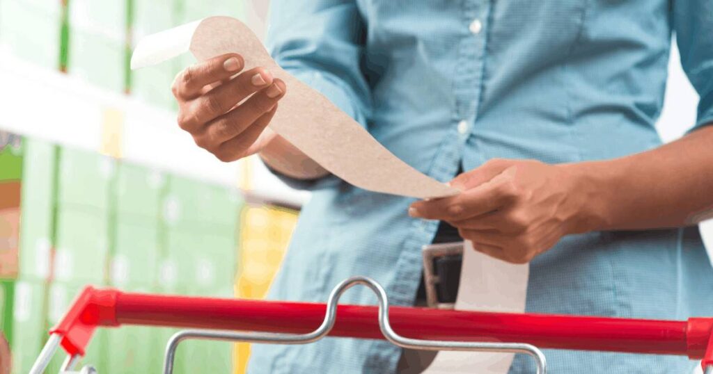 Woman reading receipt with shopping cart