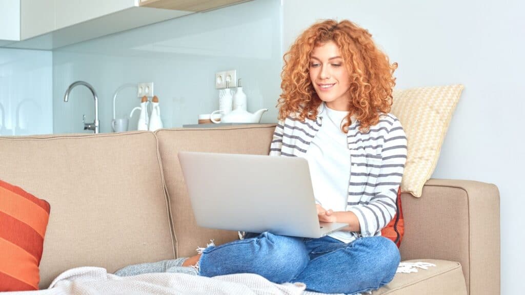 Woman working on her side hustles at home with her laptop on her couch