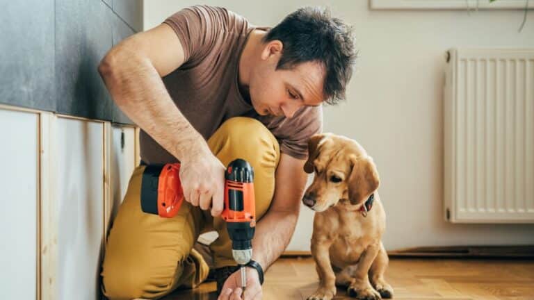 Man holding a drill working on a DIY project with a puppy next to him