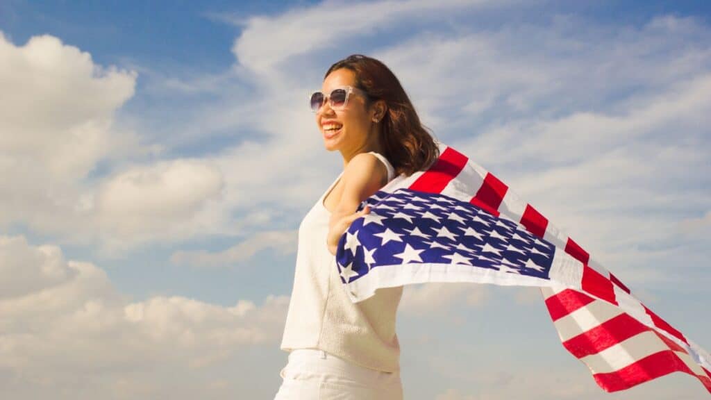 Young woman holding an American flag with clouds in the background
