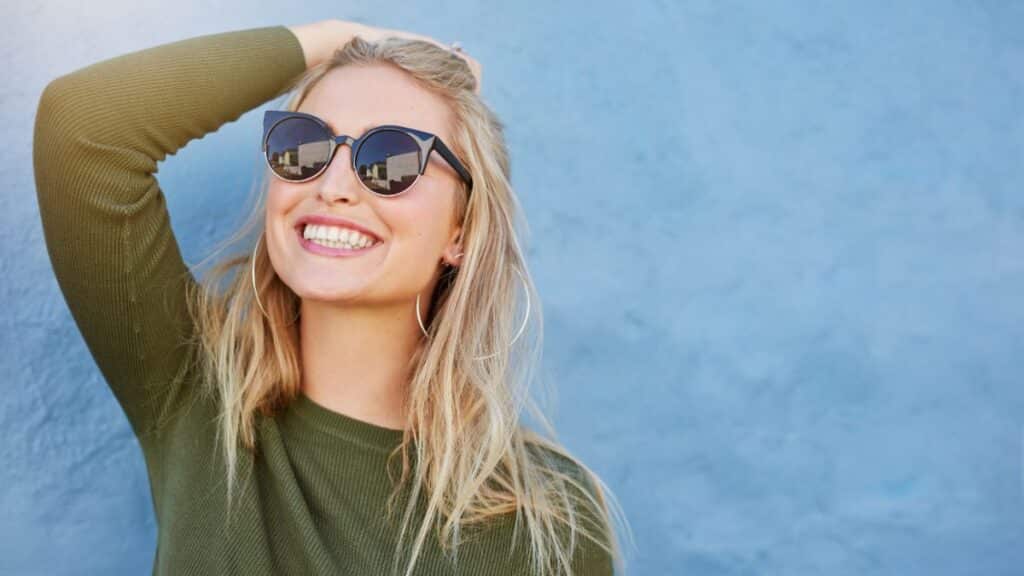 Young woman wearing sunglasses and smiling big
