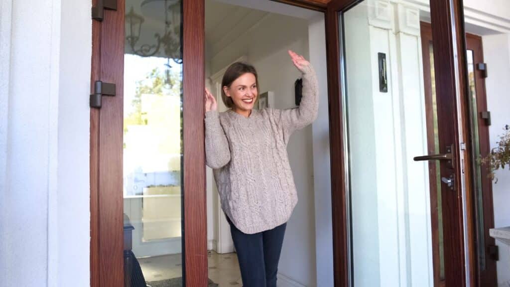 Woman standing in doorway of a house waving goodbye