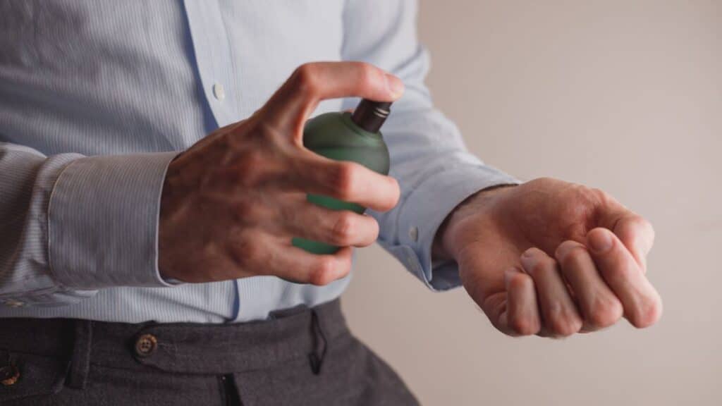 Man in dress shirt spraying cologne on his wrist