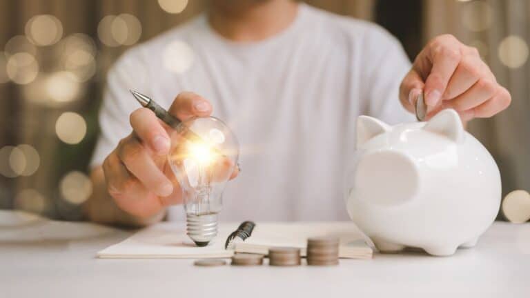 Man holding a lightbulb and saving coins in a piggy bank