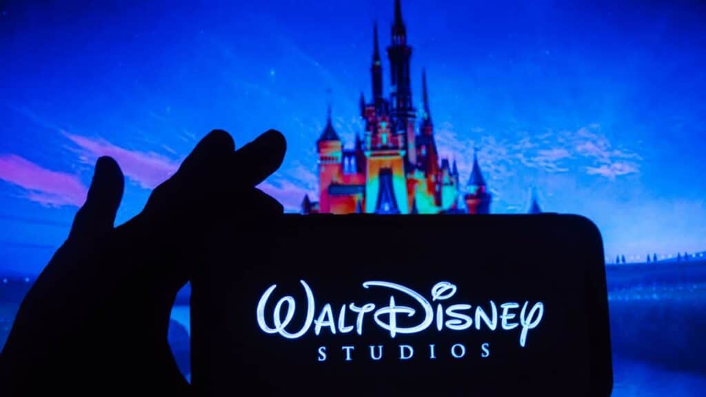 Cindarella's castle at Disney with person's hand holding phone showing Walt Disney on it