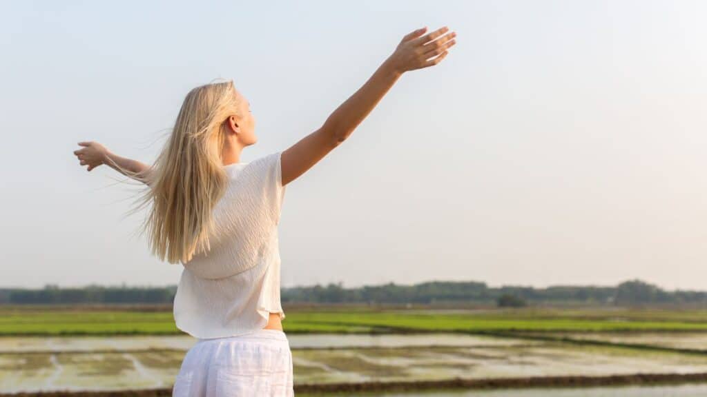 Woman standing in a field with her arms up looking happy