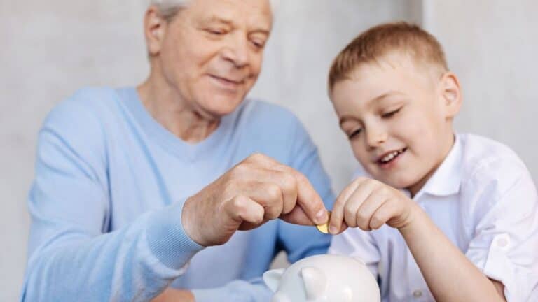 Older man putting coins into a piggy bank with a young boy
