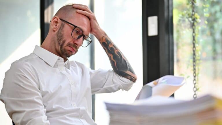 Middle aged man holding his head with tattoos looking upset