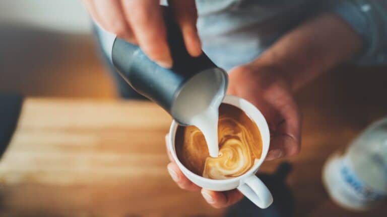 Barista pouring milk in coffee