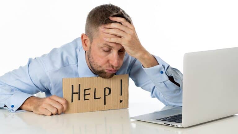 Man looking frustrated with his laptop and holding a sign that says "help"