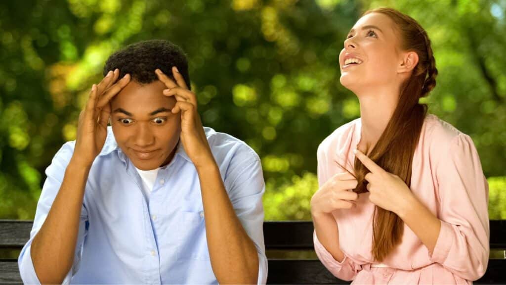 Young couple sitting on a bench outside with the man seeming to be annoyed
