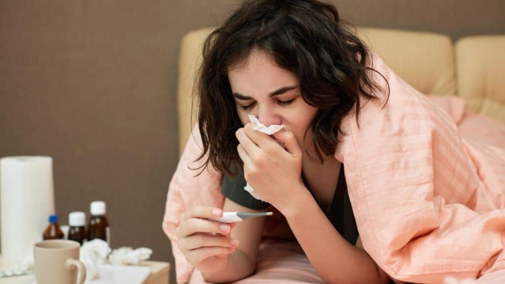 Sick woman in bed blowing her nose and taking her temperature