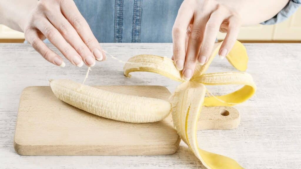 Person peeling a banana on a cutting board and peeling the strings off