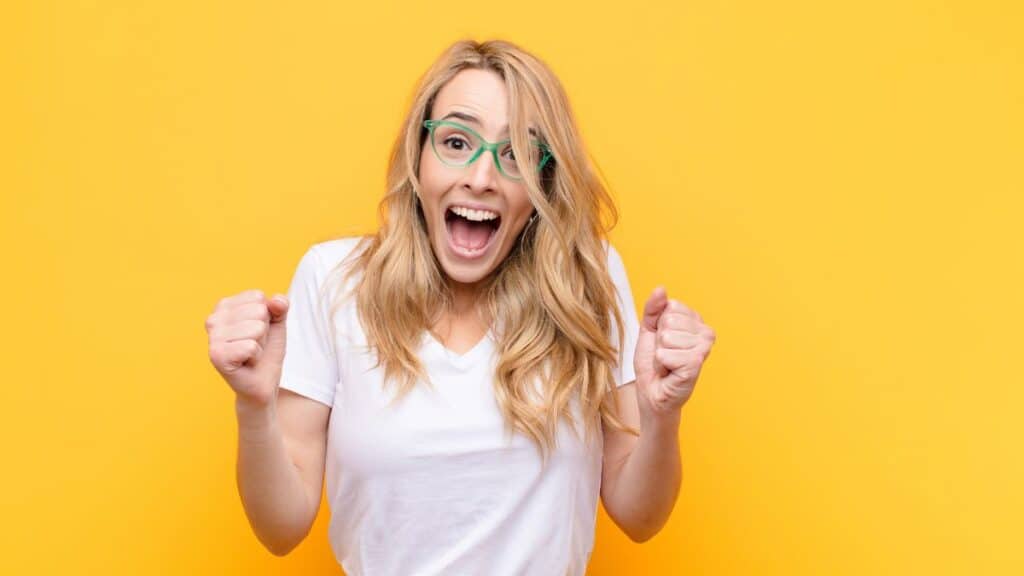 Excited young blonde wearing glasses on yellow background