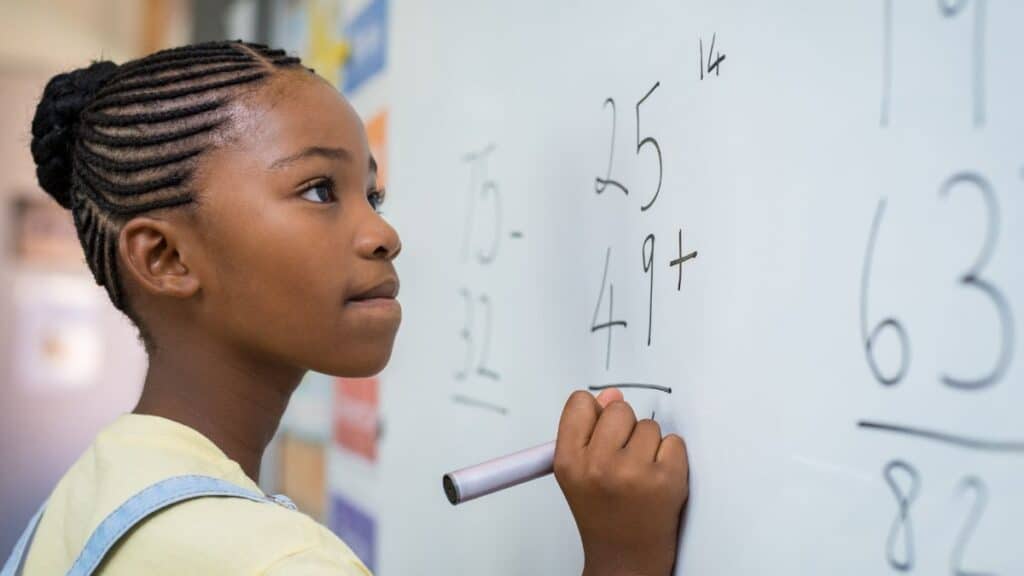 Young girl doing math on a white board in her gifted class