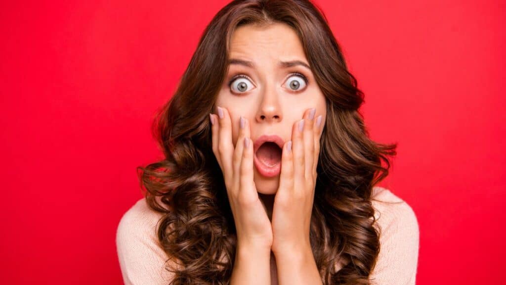 Woman looking wide-eyed and scared with hands to face