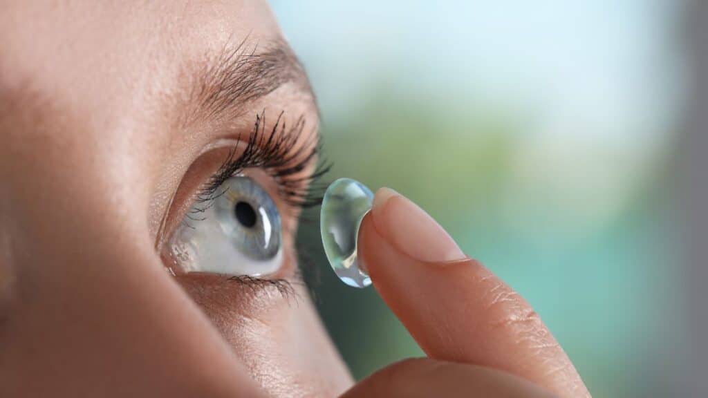 Woman holding a contact lens on her finger and placing it on her eye