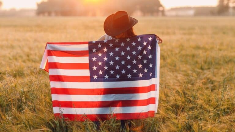 Cowgirl standing in a field holding an American flag on her back