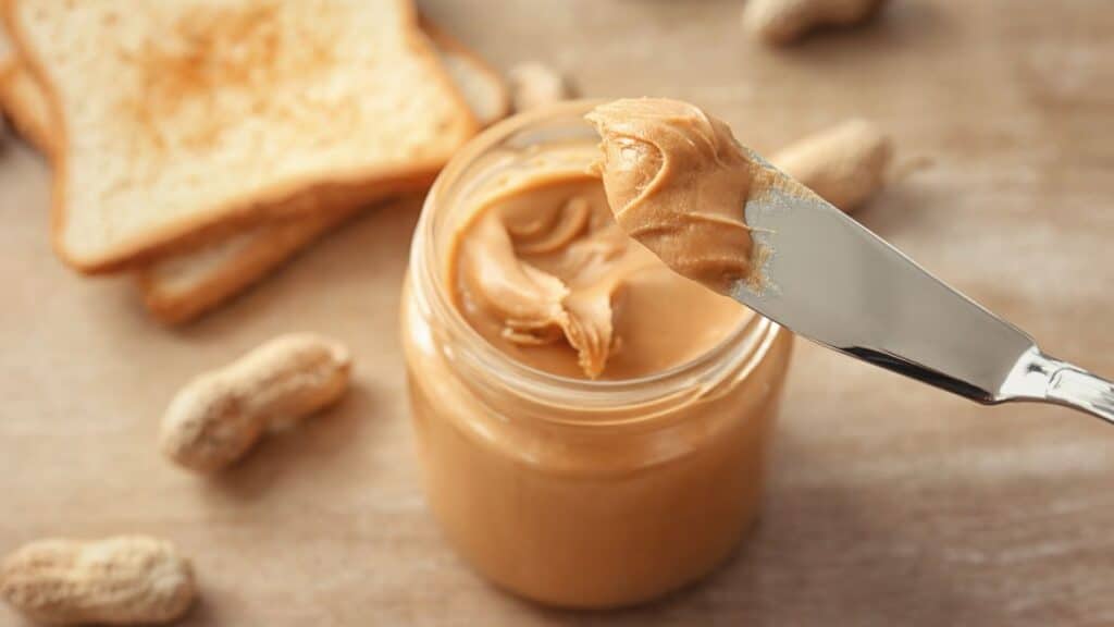 Jar of peanut butter with peanuts and toast