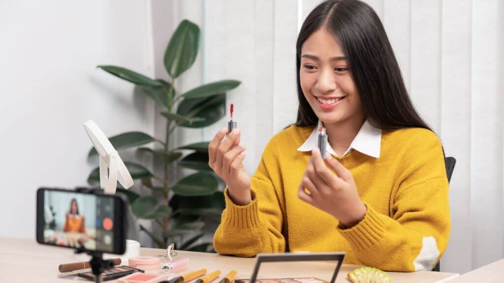Asian woman recording herself showing different cosmetics.