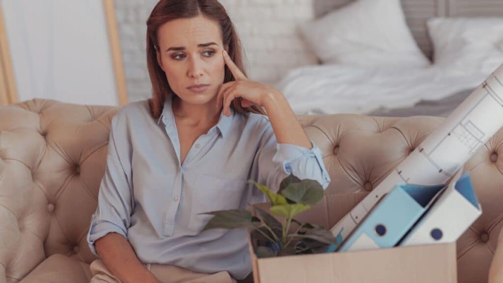 Woman sitting on couch with a box of her belongings looking sad like she lost her job