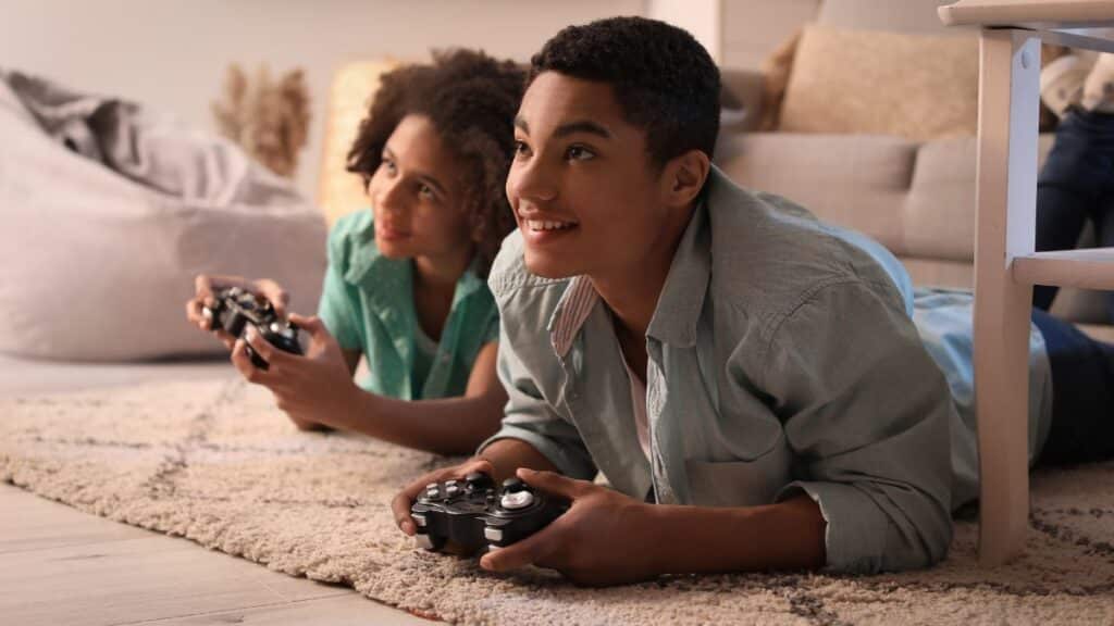Young boys playing video games while laying on the floor.