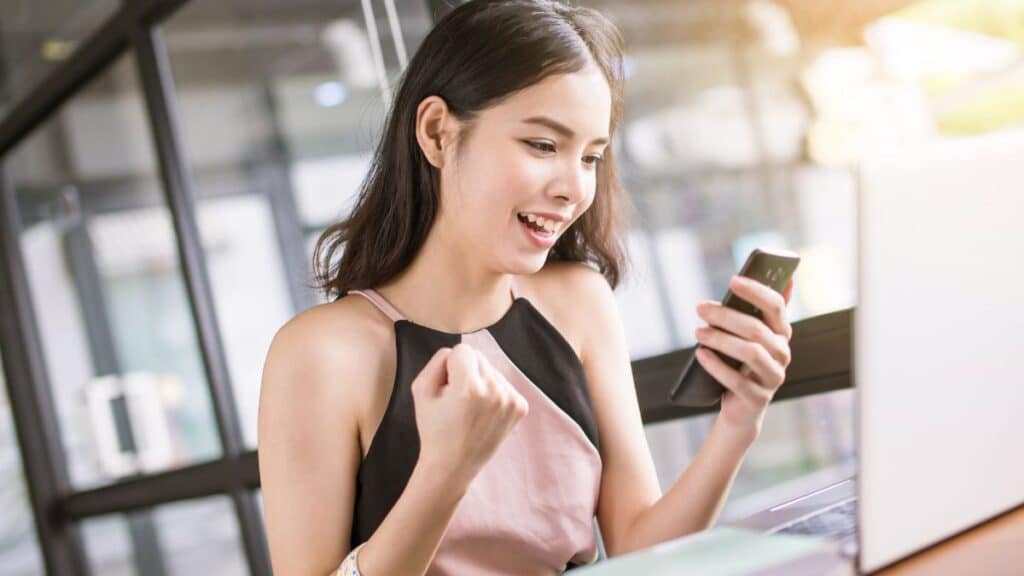 Young woman cheering while looking at her phone