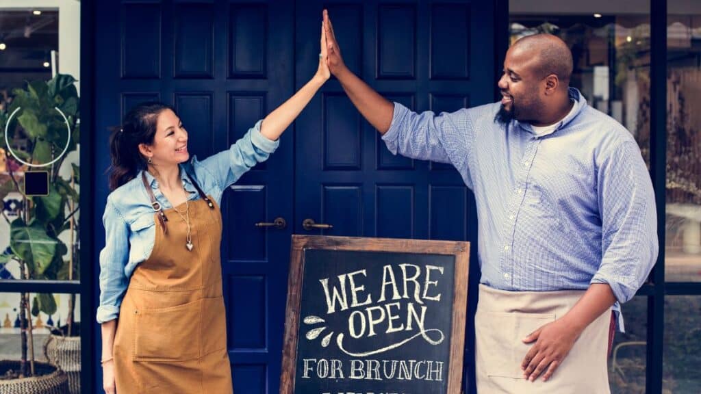 Business owners high-fiving each other above a sign for a restaurant grand opening