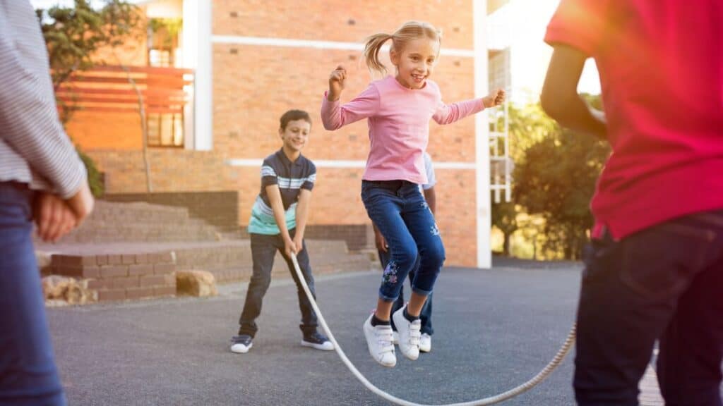 A group of young kids playing jump rope outside.