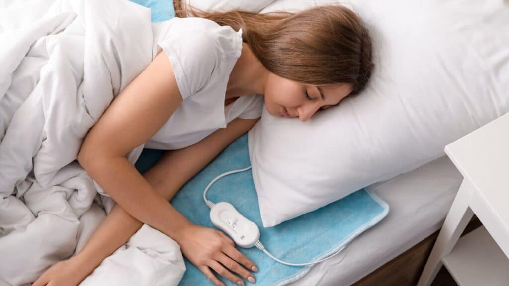 A young woman sleeping on an electric heating pad in bedroom.