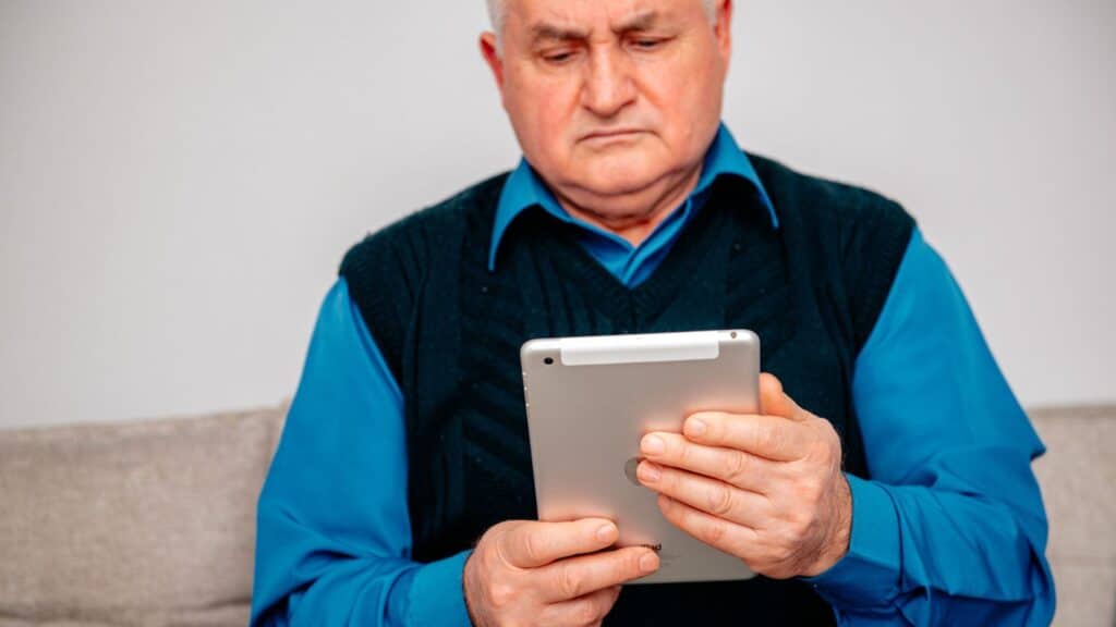 Older man looking annoyed while using a tablet