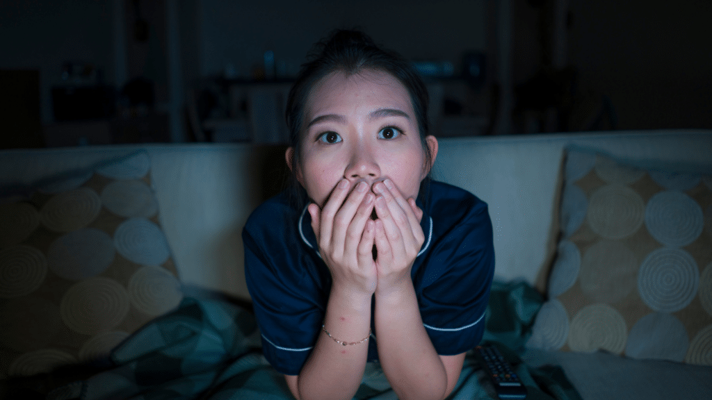 Young woman looking at something with her hands covering her mouth like she's scared