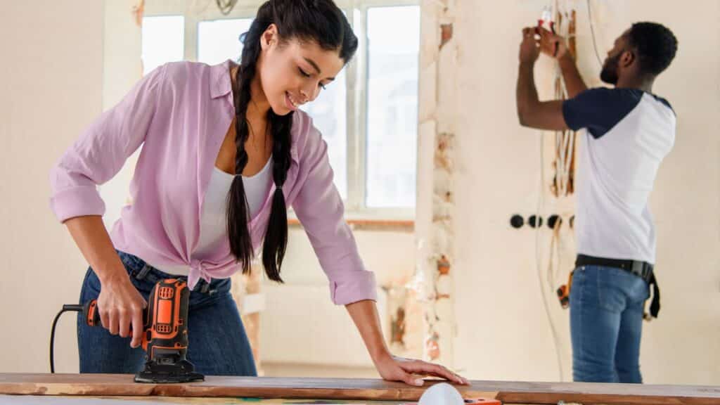 Woman sanding a board while man works in background