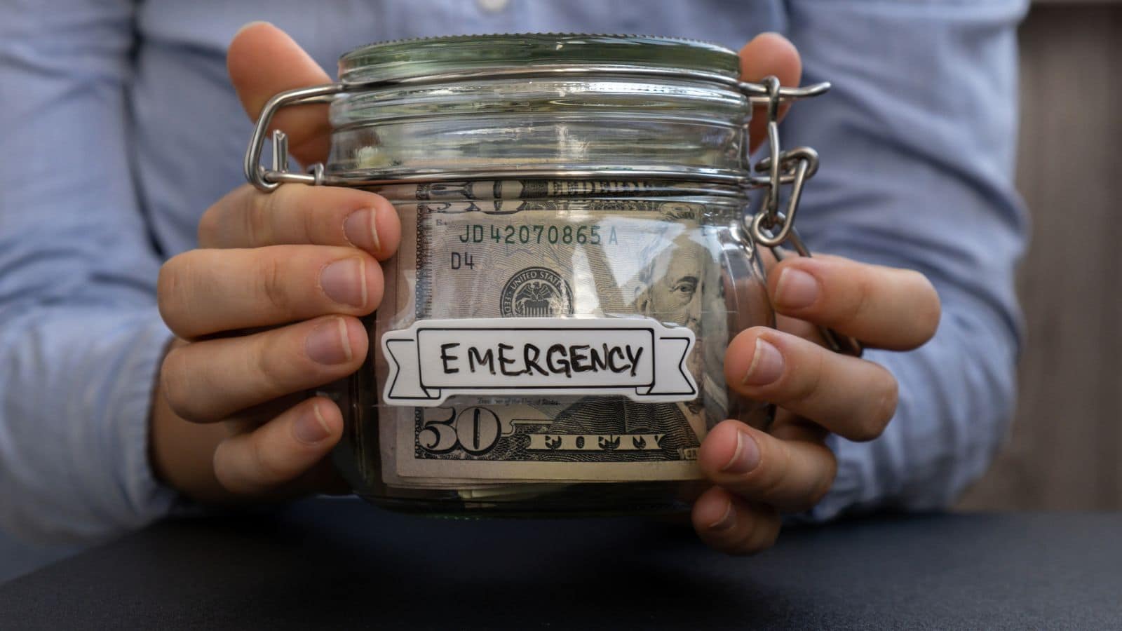 Man holding a jar filled with money and labeled "emergency"