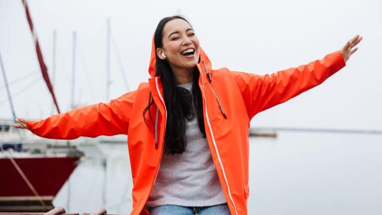 Young woman wearing a red jacket smiling with her arms out