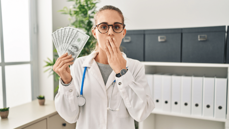 Young female doctor covering her mouth and holding a handful of cash