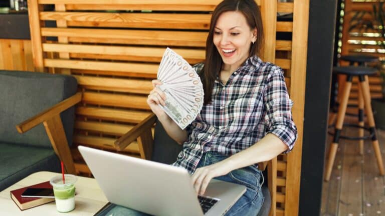 Young woman working on her laptop holding a handful of money