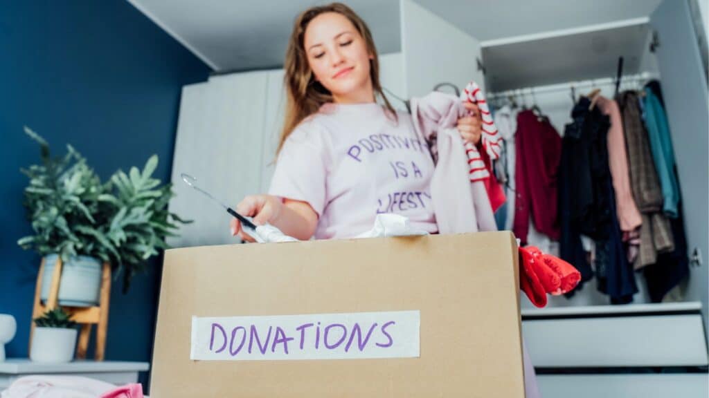 Young woman decluttering and putting clothing in a donation