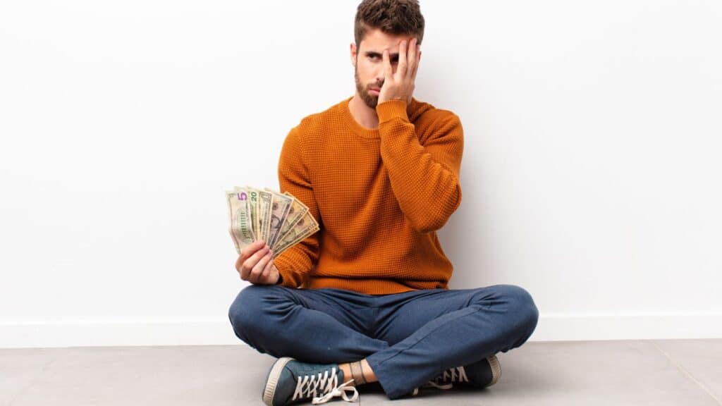 Man sitting on the floor with his hand on his face and holding money