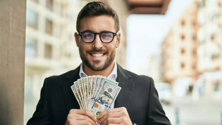 Man in suit and glasses smiling and holding cash