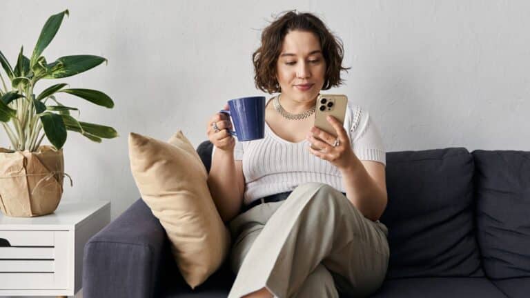 Minimalist woman sitting on the couch drinking coffee and using her phone