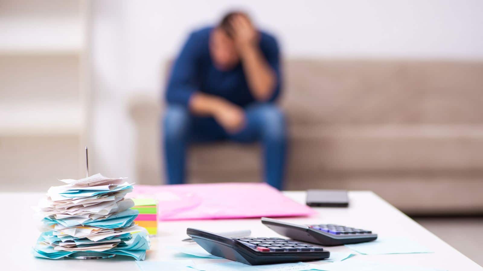 Man sitting on the couch stressed with a pile of unpaid bills