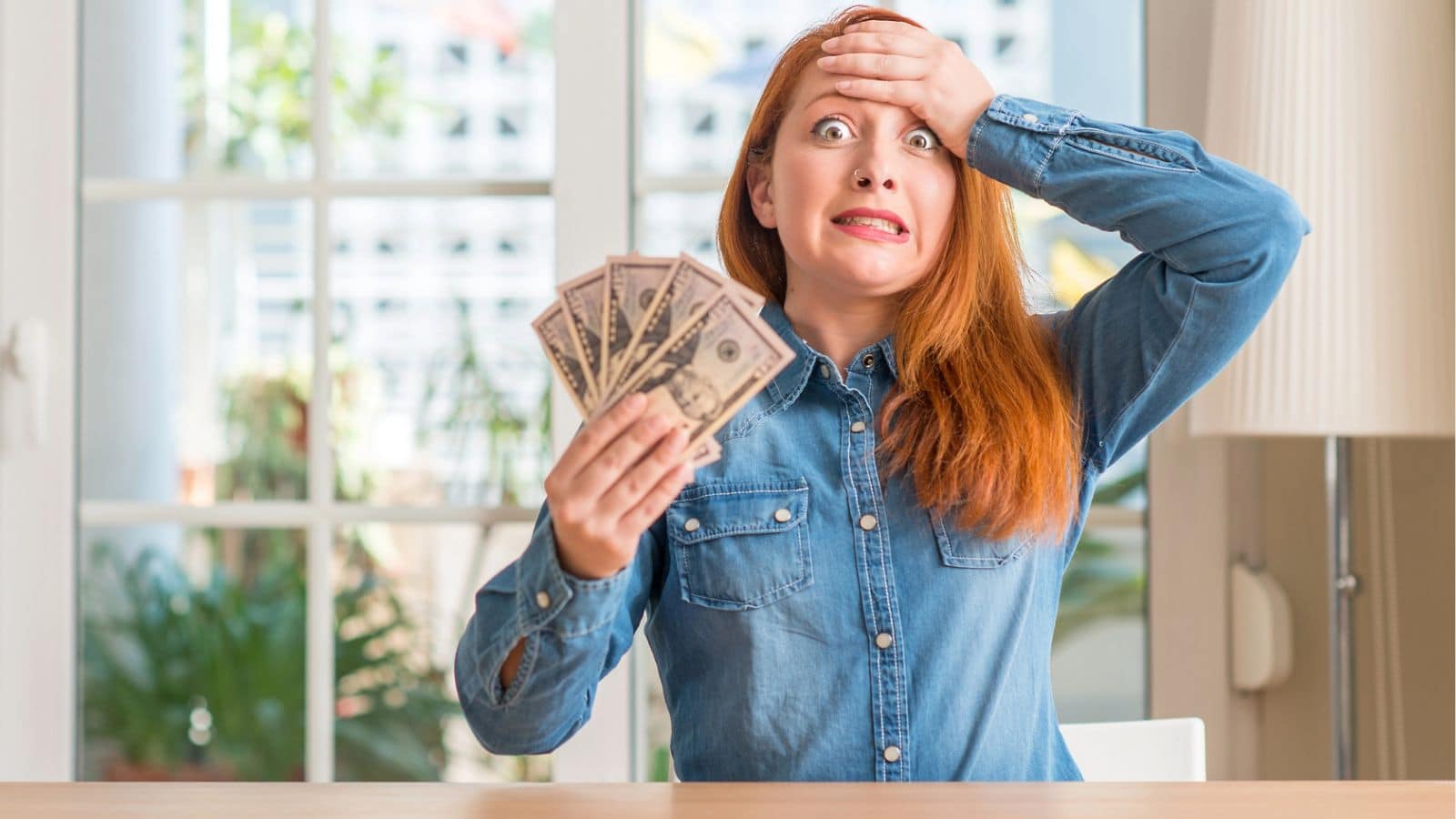 Redhead woman holding money and looking scared