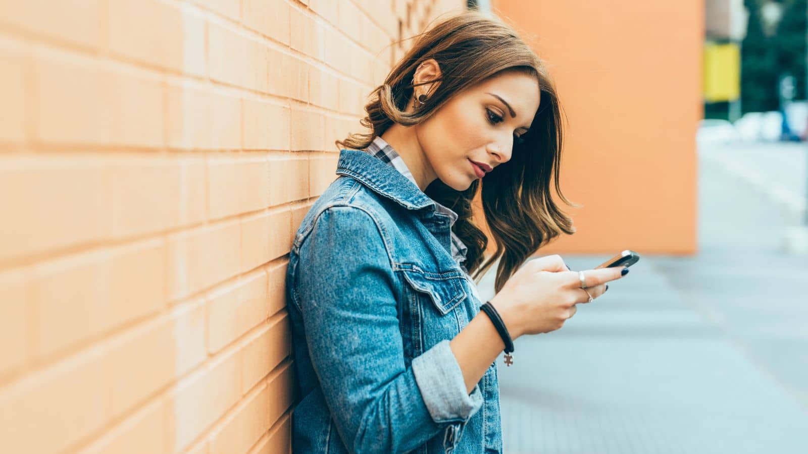 Gen-Z woman leaning against a wall and looking at her phone