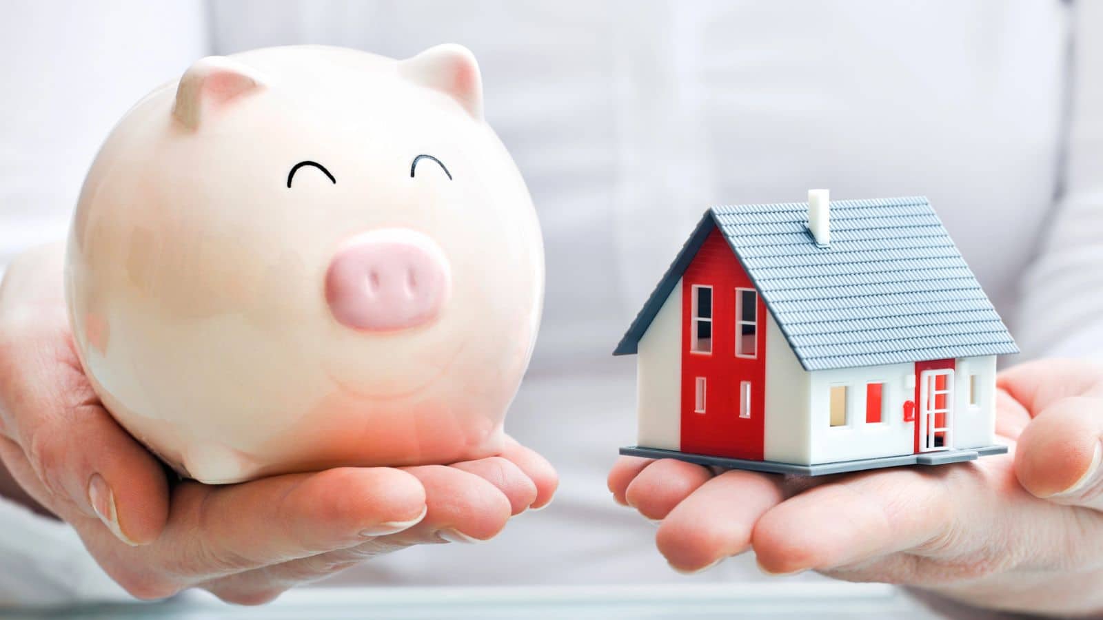 Person holding a piggy bank in one hand and a house in the other