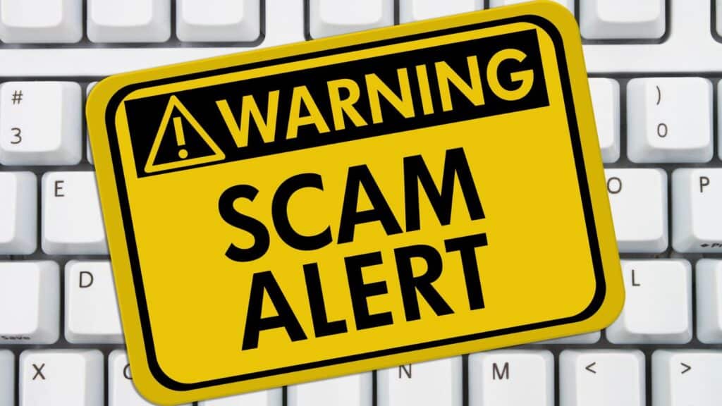 Computer keyboard with yellow sticker that reads: warning scam alert"