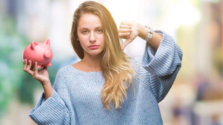 Young woman holding a piggy bank and giving a thumbs down