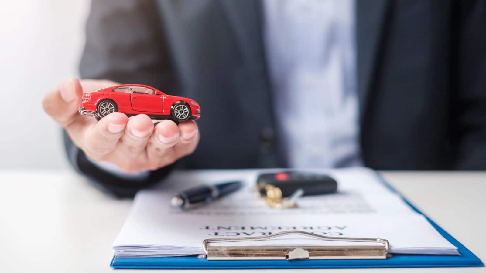 Car salesman holding a toy car while working with a customer for a loan application